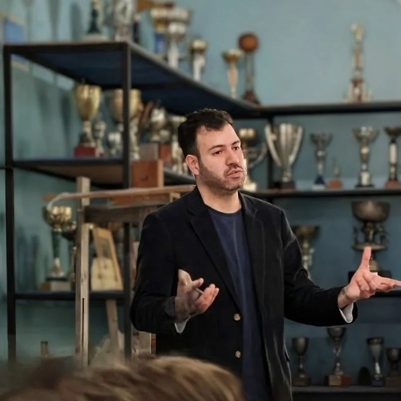 Nicolás Olave gesticulando durante la charla, con trofeos antiguos de fondo